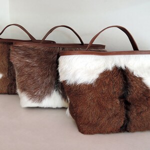 May include: Three brown and white cowhide tote bags with brown leather handles.