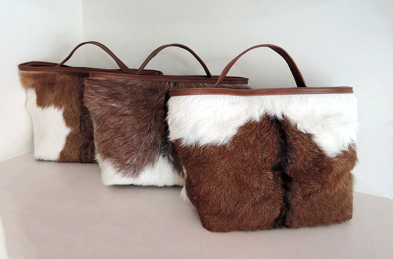 May include: Three brown and white cowhide tote bags with brown leather handles.