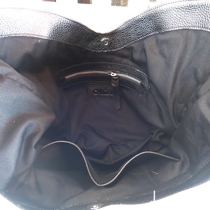 Puede incluir: Un bolso tote de cuero negro con exterior texturizado y forro interior de tela negra lisa. El bolso cuenta con un cierre magn&eacute;tico a presi&oacute;n en la parte superior, un bolsillo interior con cremallera y un bolsillo abierto en la parte inferior.