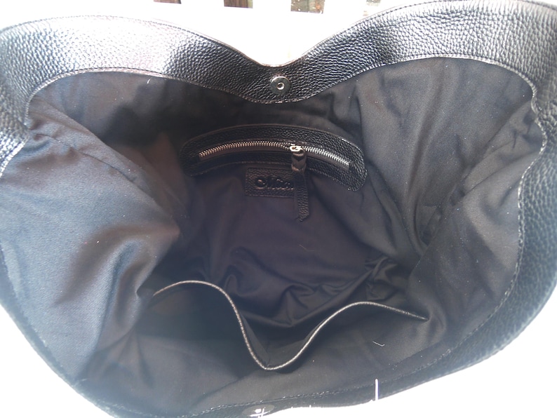 Puede incluir: Un bolso tote de cuero negro con exterior texturizado y forro interior de tela negra lisa. El bolso cuenta con un cierre magn&eacute;tico a presi&oacute;n en la parte superior, un bolsillo interior con cremallera y un bolsillo abierto en la parte inferior.