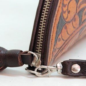 May include: A brown leather wallet with a zipper closure and a tassel. The wallet has a floral design and a silver clasp.