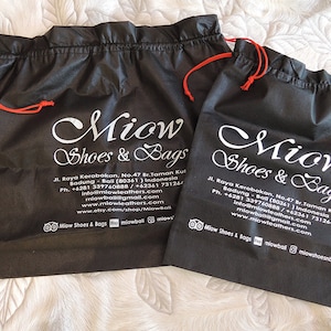 May include: Two black drawstring bags with white text that reads "Miow Shoes & Bags" and contact information. The bags have red drawstrings.
