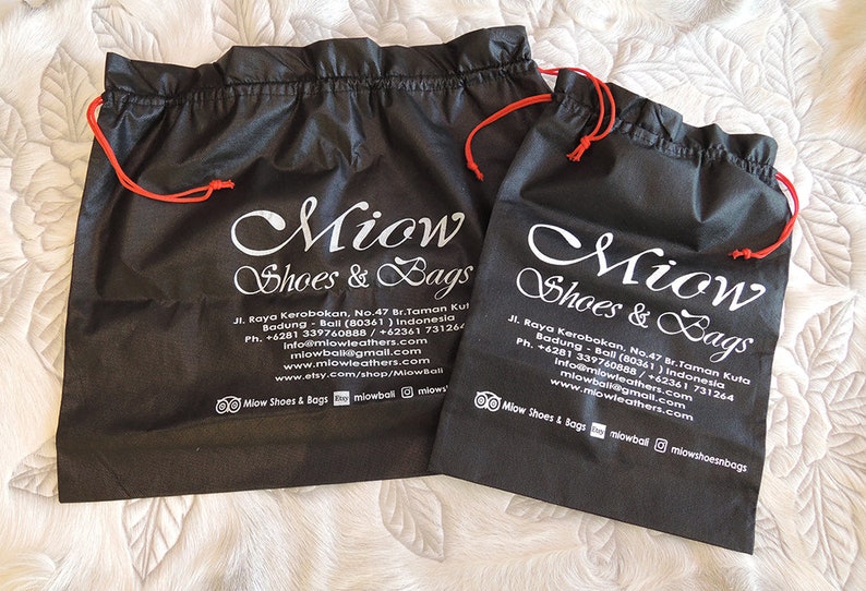 May include: Two black drawstring bags with white text that reads "Miow Shoes & Bags" and contact information. The bags have red drawstrings.