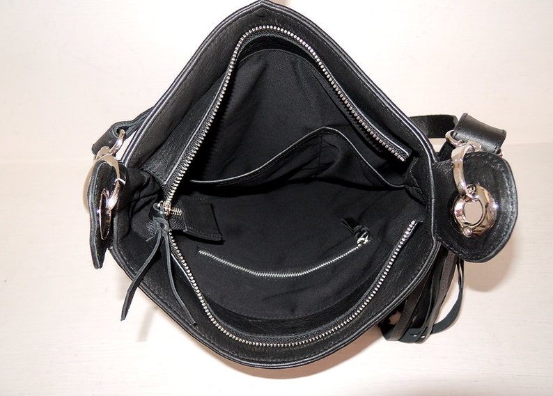 May include: Black leather shoulder bag with a silver zip and a silver ring on the strap. The bag has a flap closure and a small pocket on the inside.