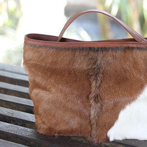 May include: A brown and white cowhide tote bag with a brown leather handle.
