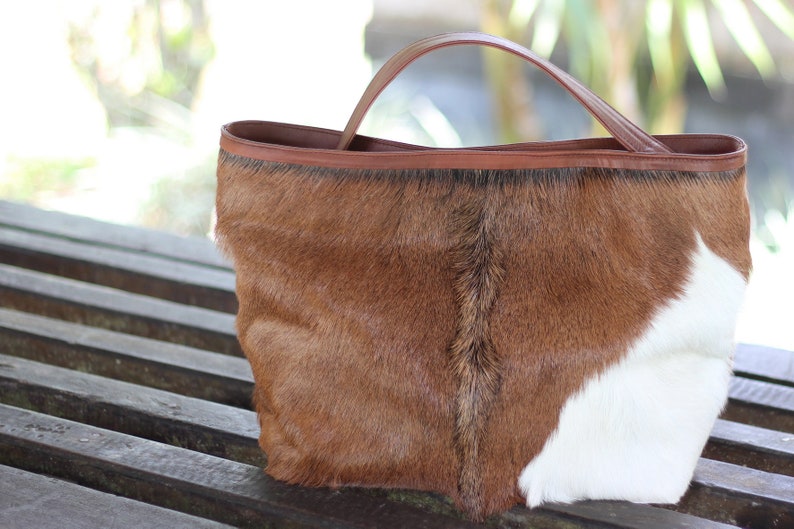 May include: A brown and white cowhide tote bag with a brown leather handle.