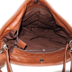 May include: A brown leather shoulder bag with a zipper closure and a flap. The bag has a brown lining and a small pocket inside. The bag has a long adjustable strap.
