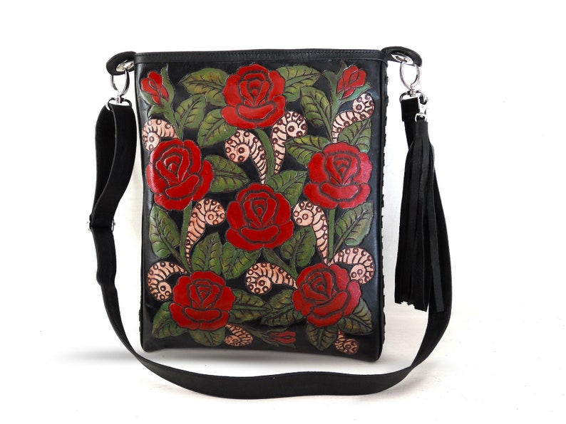 May include: Black leather shoulder bag with a floral design featuring red roses and green leaves. The bag has a long adjustable strap and a tassel.