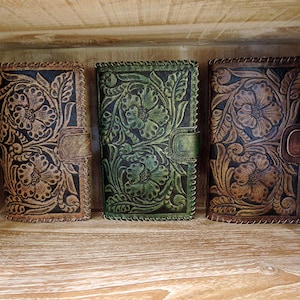 May include: Three leather wallets with floral embossed designs. The wallets are brown, green, and brown with black accents.
