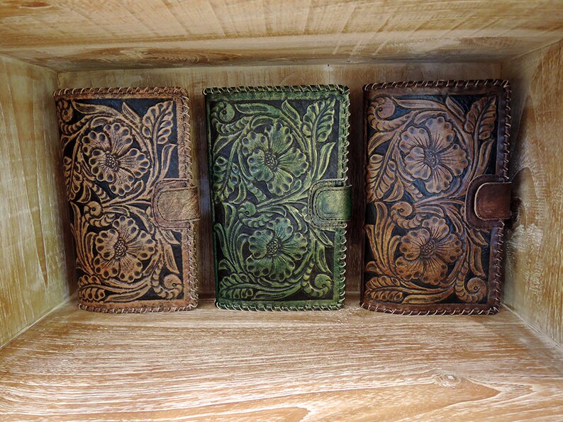 May include: Three leather wallets with floral embossed designs. The wallets are brown, green, and brown with black accents.