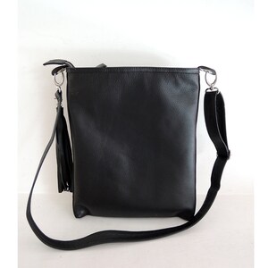 May include: A black leather shoulder bag with a long strap and a tassel. The bag has a simple design and is made of high-quality leather.