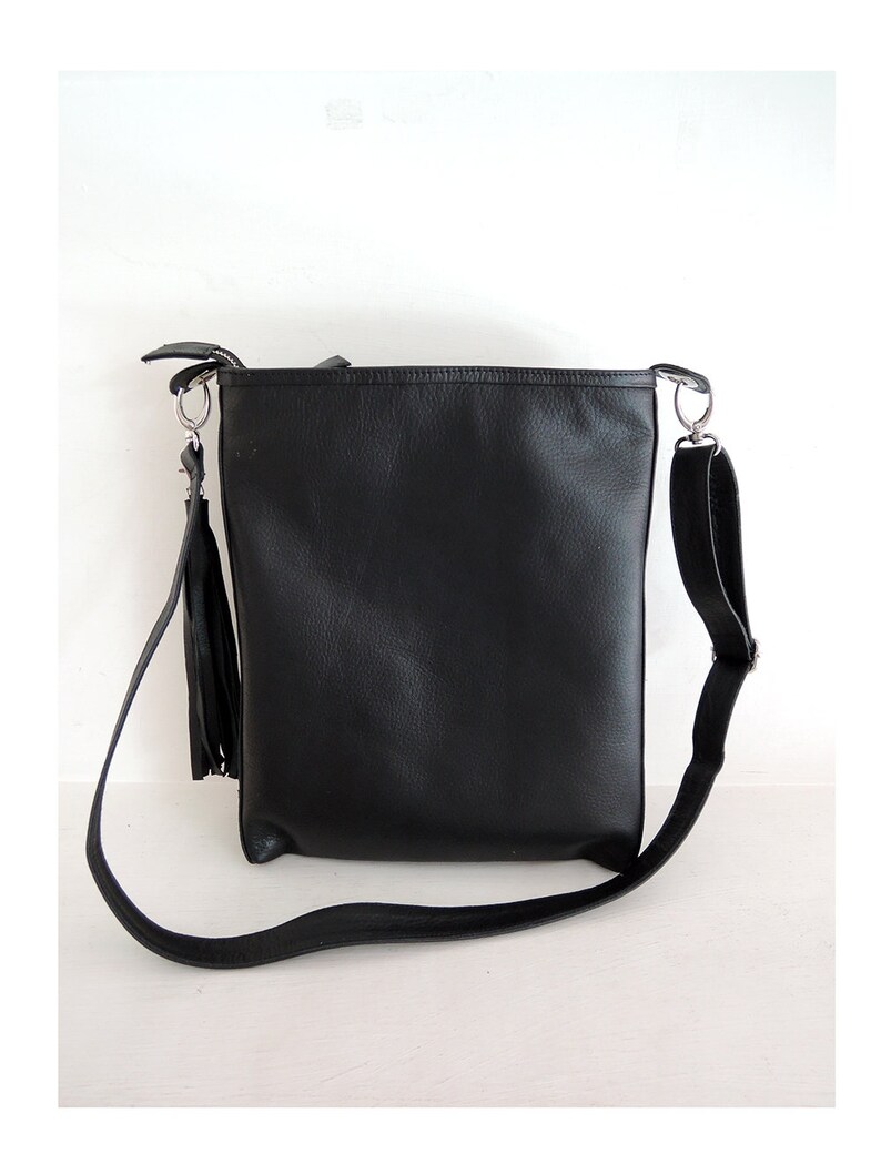 May include: A black leather shoulder bag with a long strap and a tassel. The bag has a simple design and is made of high-quality leather.