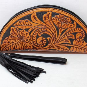 May include: A half-moon shaped leather clutch with a black tassel. The clutch is decorated with a tooled floral design in brown on a black background.