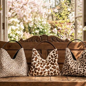 Puede incluir: Tres bolsos de estilo hobo con estampados de animales. Los bolsos de la izquierda y la derecha tienen un dise&ntilde;o de puntos negros sobre fondo crema, mientras que el central muestra un estampado de leopardo marr&oacute;n y blanco. Cada bolso tiene un asa.