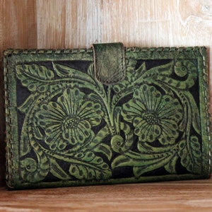 May include: A green leather wallet with a floral embossed design. The wallet has a flap closure and a stitched edge.