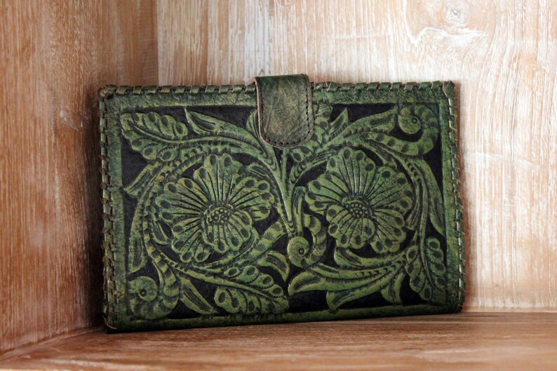 May include: A green leather wallet with a floral embossed design. The wallet has a flap closure and a stitched edge.