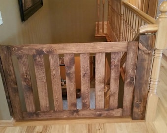 May include: A rectangular wooden safety gate featuring a dark brown stained finish with visible wood grain patterns. The gate is constructed with a horizontal top and bottom rail and six vertical slats, secured to a wooden post at the staircase.