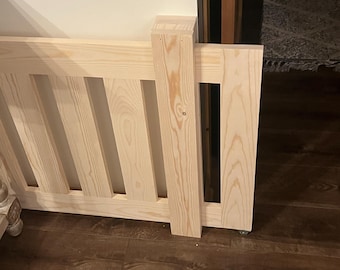 May include: A light-colored wooden gate featuring vertical slats and a solid central post. The gate is constructed from natural pine wood with visible grain patterns and is designed to be positioned across a doorway or opening.