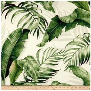 May include: A white fabric with a green tropical leaf pattern. The leaves are large and have a realistic look.