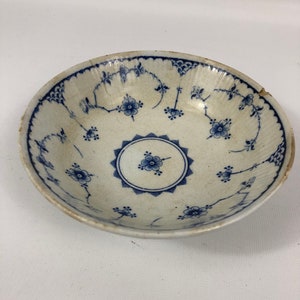 May include: A white ceramic bowl with a blue and white floral pattern. The bowl has a scalloped edge and a slightly raised center.