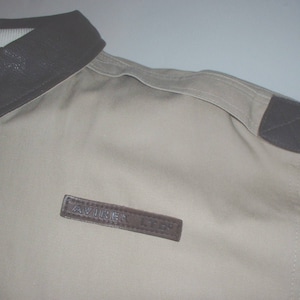 May include: A beige jacket with a brown leather collar and a brown leather patch on the shoulder. The patch has the word "AVIREX" on it.