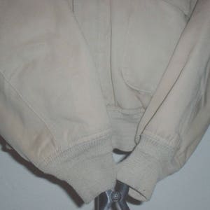 May include: A beige jacket with a ribbed knit cuff on each sleeve. The jacket is made of a soft, lightweight fabric.