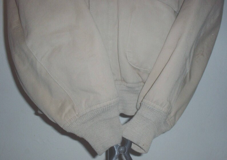 May include: A beige jacket with a ribbed knit cuff on each sleeve. The jacket is made of a soft, lightweight fabric.