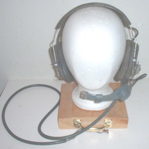 May include: Gray noise-canceling headphones with a boom microphone and a gray cord. The headphones are on a wooden stand.