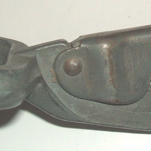 May include: A close-up of a metal hook with a swiveling ring. The hook is gray and has a smooth, slightly worn finish.