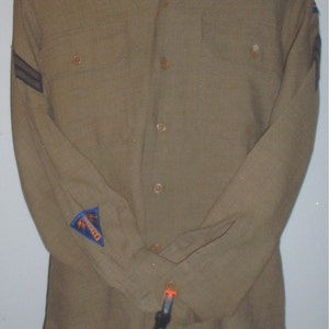 May include: A brown long-sleeved shirt with two black stripes on the left sleeve and a blue patch with a white symbol on the left sleeve.