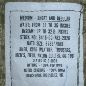May include: A white tag with black text detailing the size and specifications of a medium, short and regular cold weather liner. The tag reads "MEDIUM - SHORT AND REGULAR", "WAIST: FROM 31 TO 35 INCHES", "INSEAM: UP TO 32 1/2 INCHES", "STOCK NO: 8415-00-782-2926", "NATO SIZE: 6783/7989", "LINER, COLD WEATHER, TROUSERS, MEN'S, FIELD, NYLON QUILTED, OG-106", "DLA100-82-C-0839", "BATTING - 100% POLYESTER", "OUTER COVERING - 100% NYLON", "BENCHMARK INDUSTRIES, INC."