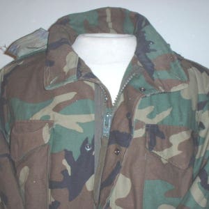 May include: A camouflage jacket with a zipper closure and a hood. The jacket has two flap pockets on the front.