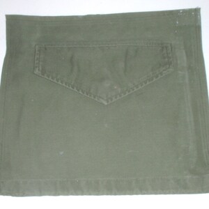 May include: A green canvas utility pouch with a large flap pocket on the front. The pouch has a sewn-in seam around the edges.