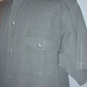 Op de afbeelding: Een olijfgroen overhemd met korte mouwen, een knoopsluiting en een enkele borstzak. Het overhemd heeft epauletten op de schouders en verticale stikseldetails. De stof lijkt een lichtgewicht materiaal te zijn.