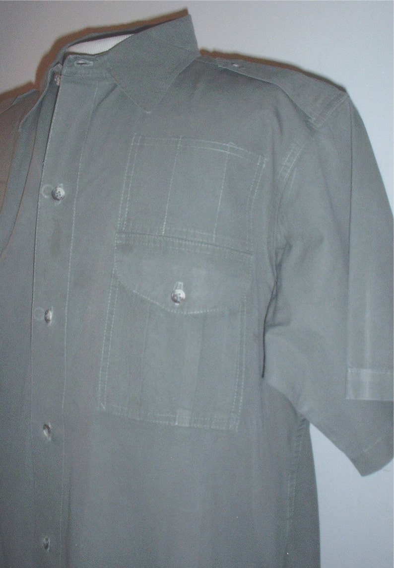 Op de afbeelding: Een olijfgroen overhemd met korte mouwen, een knoopsluiting en een enkele borstzak. Het overhemd heeft epauletten op de schouders en verticale stikseldetails. De stof lijkt een lichtgewicht materiaal te zijn.