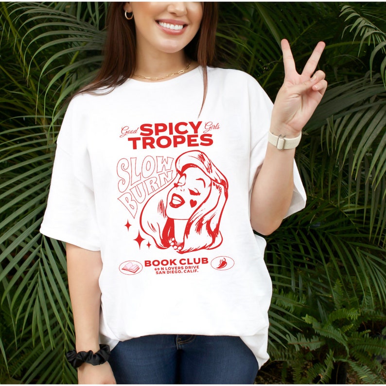 May include: White t-shirt with a red graphic design featuring a woman with the text "Good Spicy Girls Tropes Slow Burn" and "Book Club 634 N Lovers Drive San Diego, Calif".