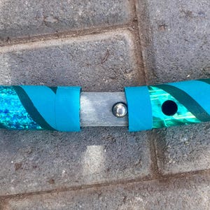 May include: A section of a teal and green hula hoop, with a connecting mechanism. The hoop has a teal and green patterned design with teal bands. The connection point is a silver metal piece with a silver button.