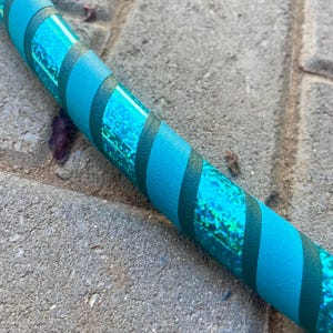 May include: A section of a teal hula hoop with a teal and dark green striped pattern. The teal sections have a glittery, iridescent finish. The hoop is designed for exercise and play.