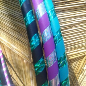 May include: A selection of colourful hula hoops with a striped design. The hoops are decorated with black, teal, purple, and silver holographic tape. The alternating colours and textures create a striking visual effect.