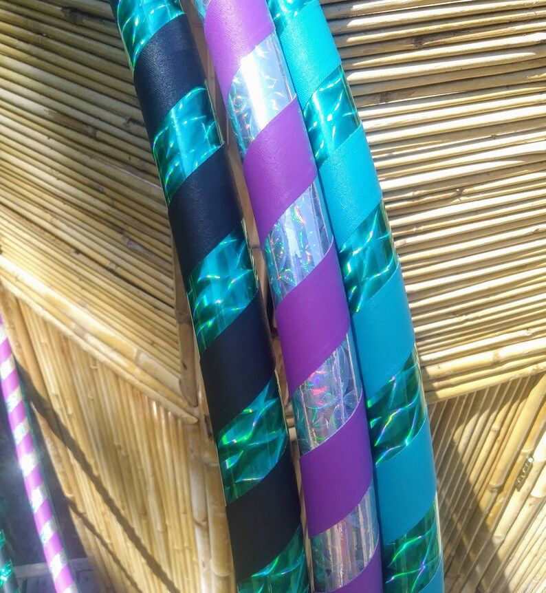May include: A selection of colourful hula hoops with a striped design. The hoops are decorated with black, teal, purple, and silver holographic tape. The alternating colours and textures create a striking visual effect.