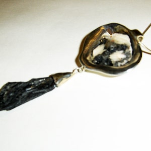 Puede incluir: Un collar de plata con un colgante de piedra negra. El colgante es una piedra negra larga y delgada con un engaste de plata. El collar est&aacute; sobre un fondo blanco.