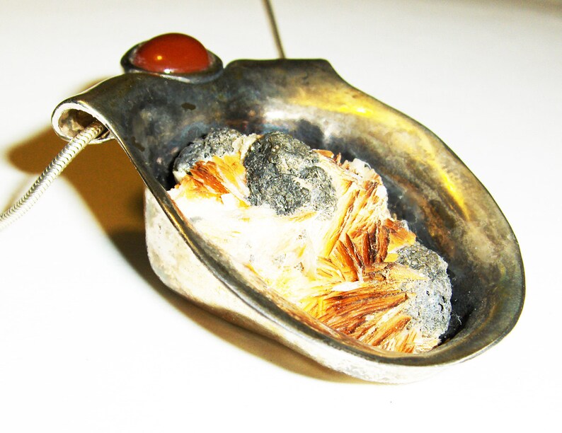May include: A silver pendant with a brown and white crystal set in a silver cup. The pendant has a red stone on the top.