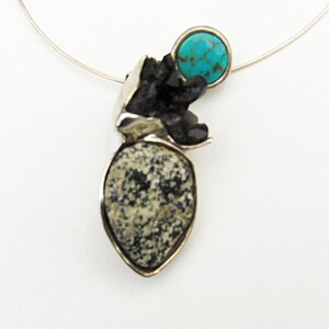 May include: A silver necklace with a pendant featuring a turquoise stone and a black and white speckled stone.
