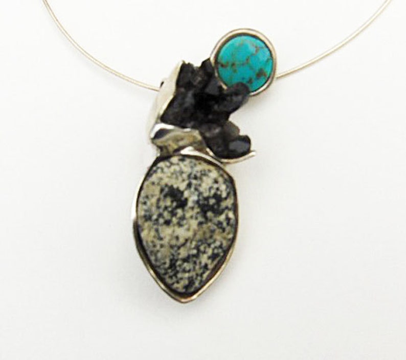 May include: A silver necklace with a pendant featuring a turquoise stone and a black and white speckled stone.