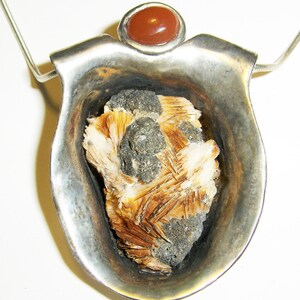 May include: A silver pendant with a brown and white crystal set in a silver cup. The pendant is topped with a red carnelian stone.