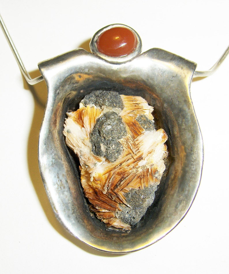 May include: A silver pendant with a brown and white crystal set in a silver cup. The pendant is topped with a red carnelian stone.