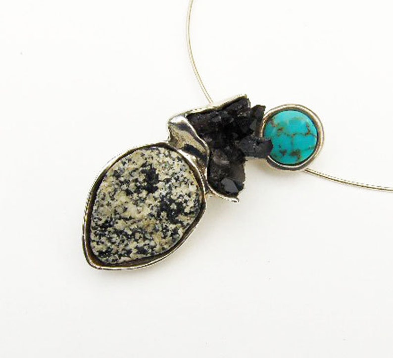 May include: A silver pendant necklace with a black and white stone, a turquoise stone, and a silver chain.