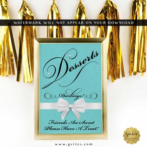 May include: A rectangular sign in a gold frame with a light blue background. The text reads "Desserts Darlings!" and "Friends Are Sweet Please Have A Treat!" in black script. A white ribbon with a bow is centered across the middle.