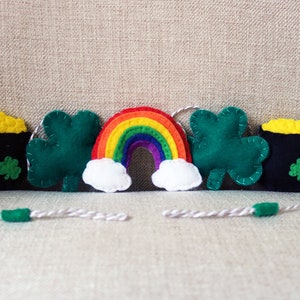 May include: A felt garland featuring shamrocks, pots of gold, and a rainbow. The garland is strung together with white twine.