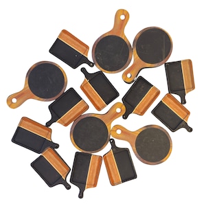 May include: A collection of small wooden serving boards with black slate surfaces. Some boards are round, others rectangular, all with wooden handles. The wood has a natural grain and a warm, brown tone, while the slate is a deep black.
